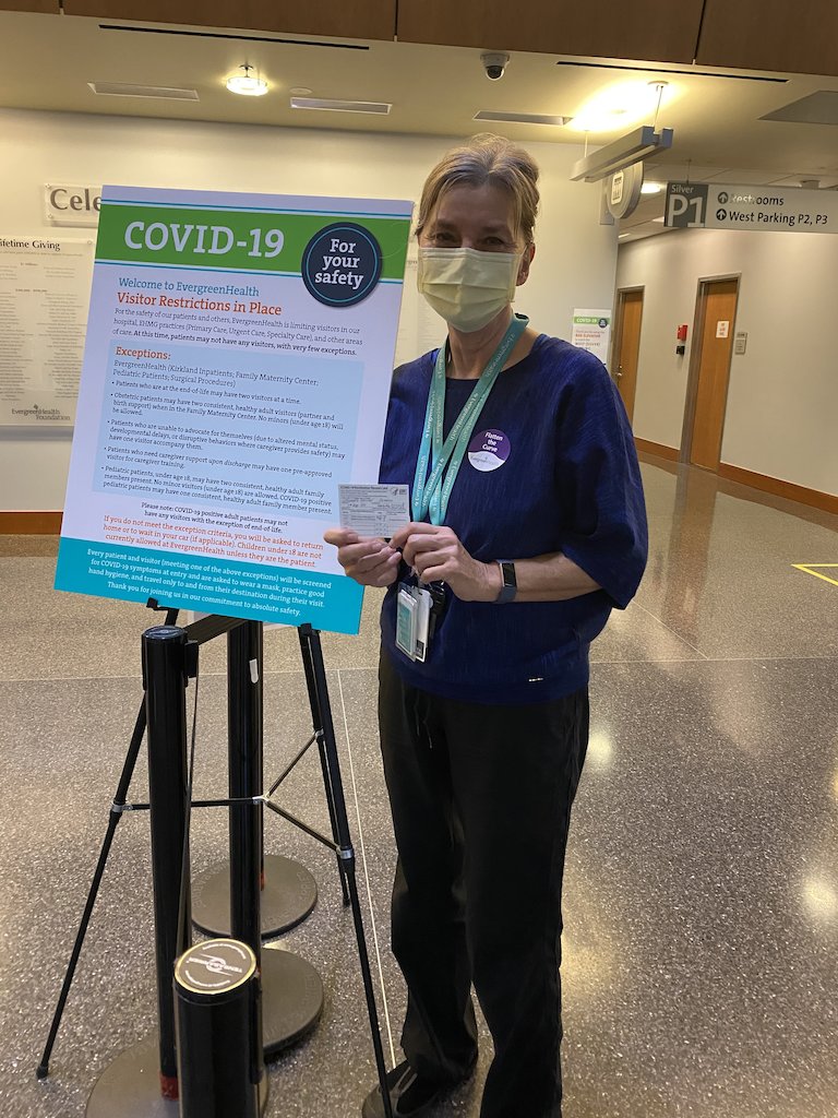 My mother, smiling with her eyes, with her COVID-19 Vaccination Record card.